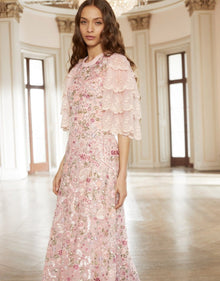  Woman wearing a modest blush pink Needle & Thread Odette Ballerina Dress gown with beaded floral embellishments and three quarter flare sleeves. 
