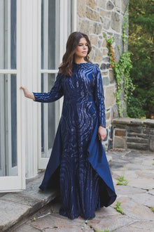  A woman wearing a modest navy blue gown with a shimmering sequin design and a removable skirt cape. The placement of the sequins is thoughtfully designed to compliment her curves.